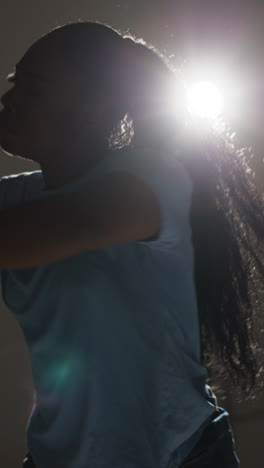 Vertical-Video-Full-Length-Studio-Portrait-Shot-Of-Young-Woman-Wearing-Hoodie-Dancing-In-Spotlight-With-Shadow-3